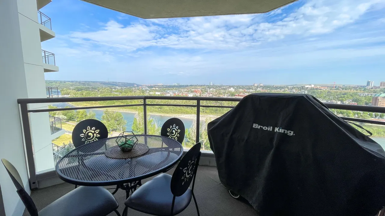 Balcony with a bistro table, chairs and a covered BBQ, overlooking the river valley