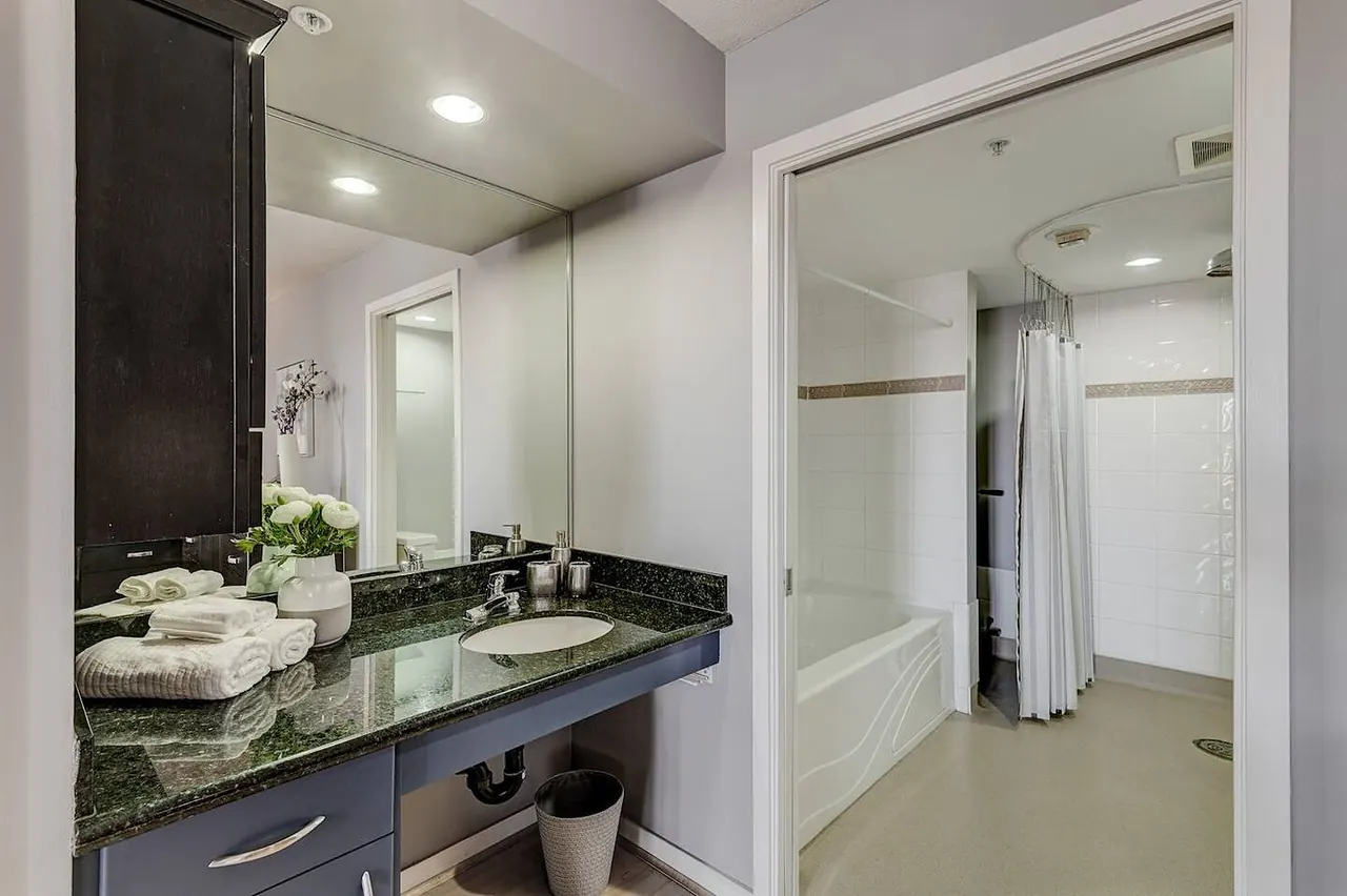 Ensuite with a granite vanity, mirror, and the tub and shower beyond