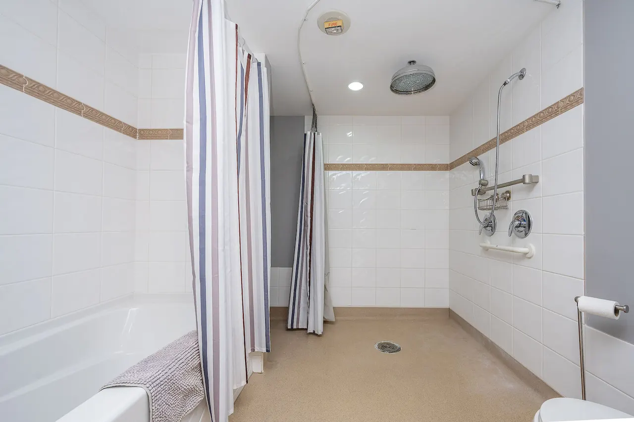 Curbless roll-in shower with a grab bar, hand shower on a slide bar and a rain head